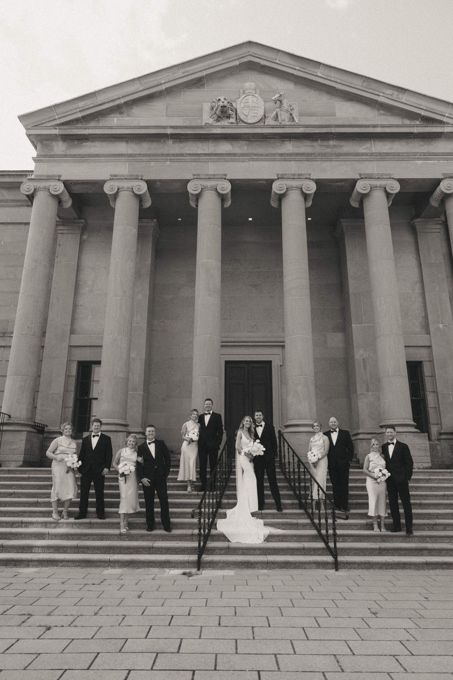 Wedding party lined up in front of a majestic neoclassical building with columns.