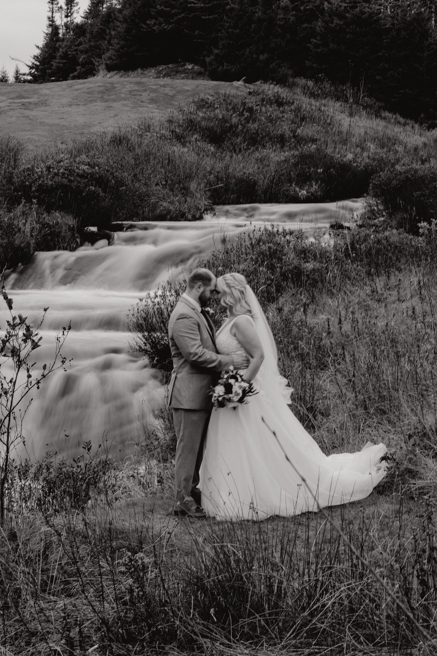 Black and white photo of a couple lying in tall grass during their wedding.