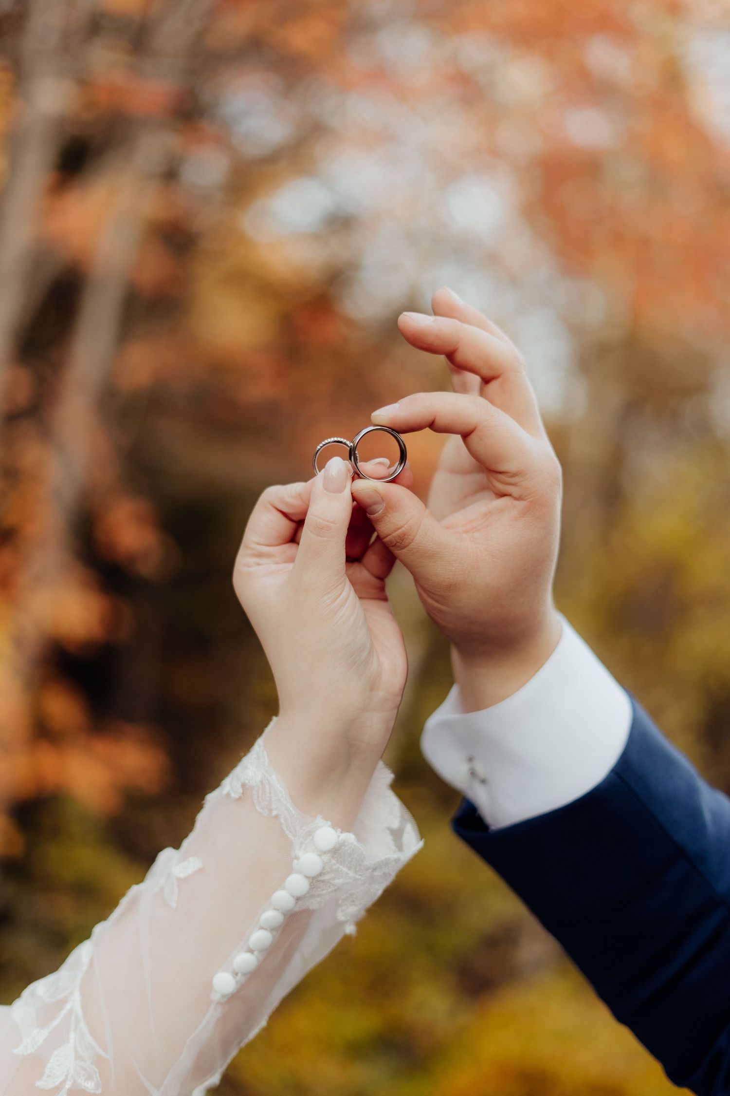 Close-up detail of hands adjusting lace wedding veil against autumn foliage.