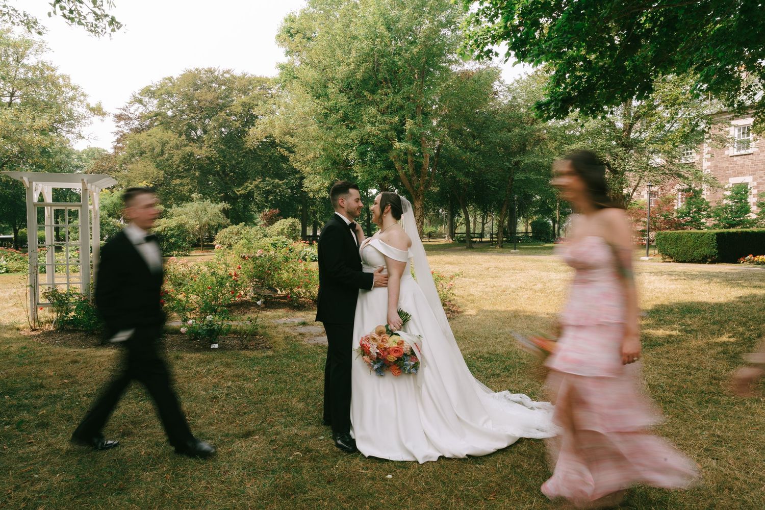 Wedding party members dance and twirl on a grassy lawn during sunset.