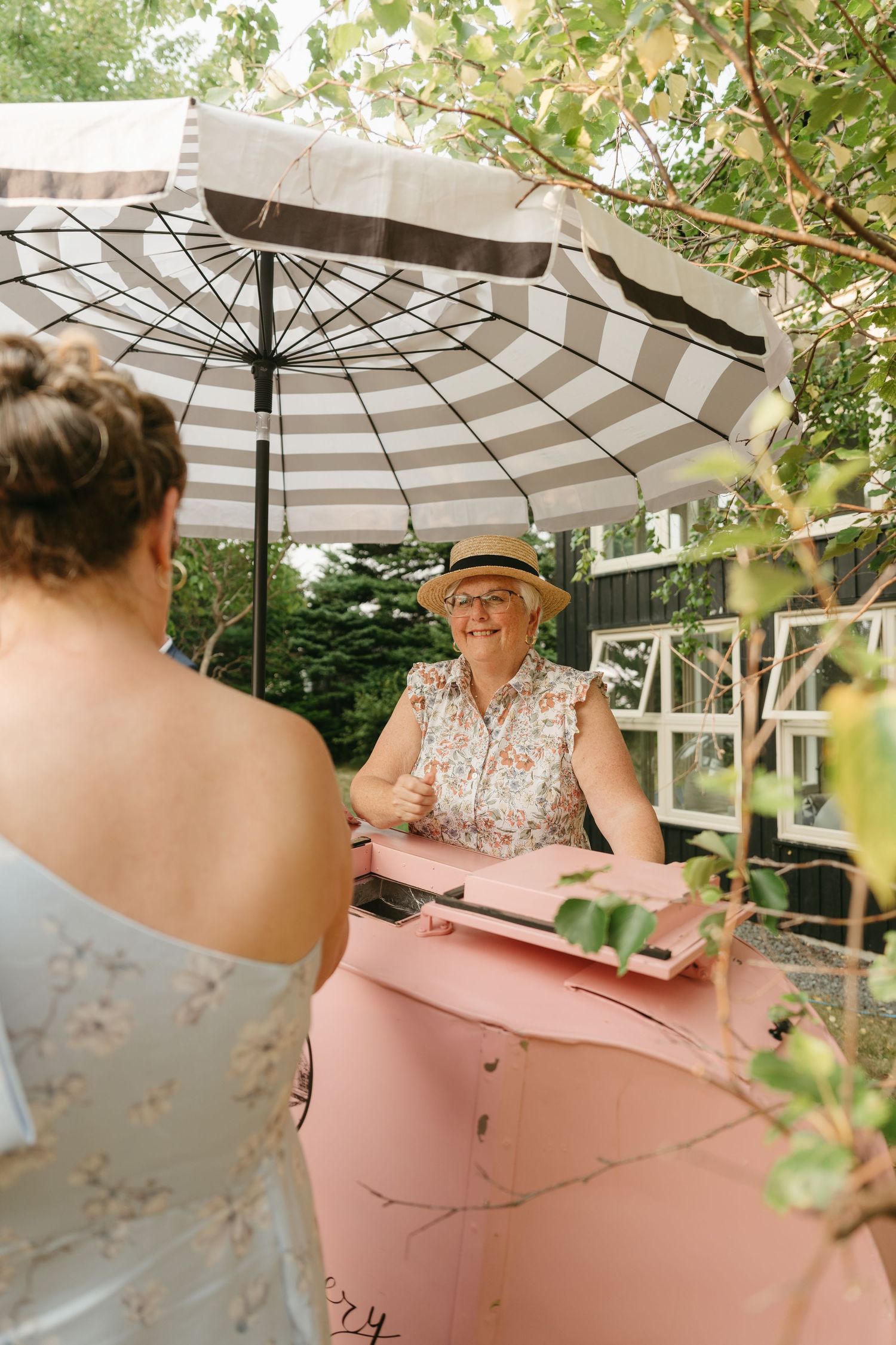 Pink vintage cart with striped umbrella set up at an outdoor garden event.