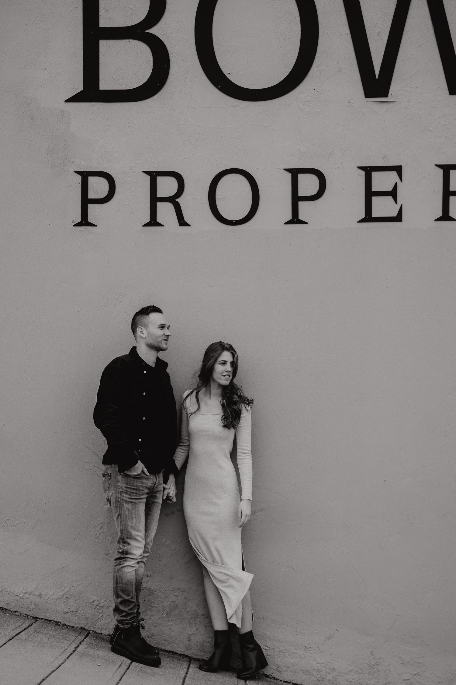 Two people leaning casually against a concrete wall with Bowring signage visible.