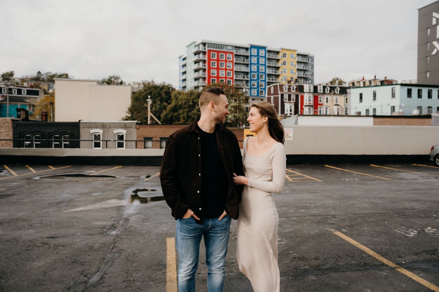A couple standing together on a rainy day in front of colorful urban architecture.
