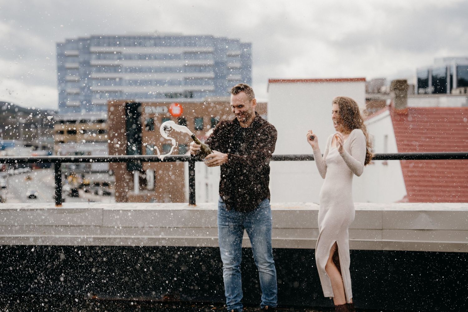 A romantic proposal scene unfolds on a city rooftop with cloudy skies overhead.