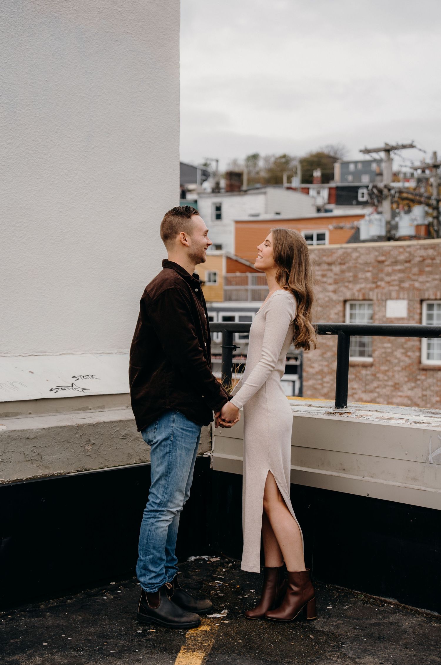 A couple shares an intimate moment on an urban rooftop surrounded by brick buildings on an overcast day.