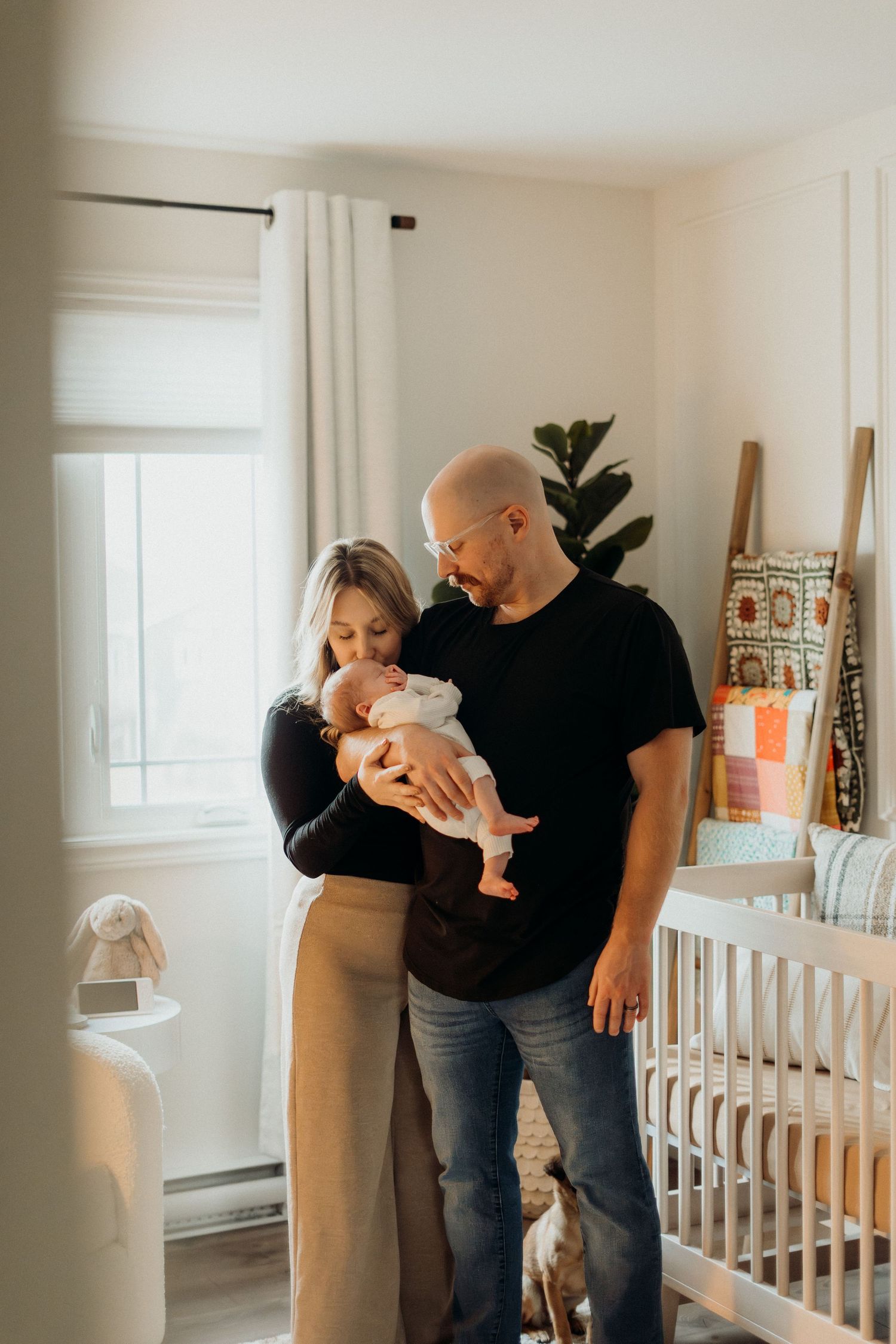 Family sharing intimate moments while holding infant in bright nursery room.