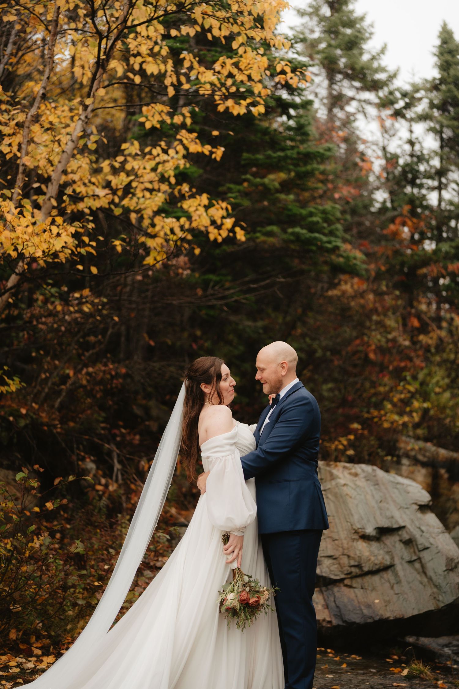 A couple shares a romantic moment during their autumn wedding surrounded by golden foliage and rocky outcrops.