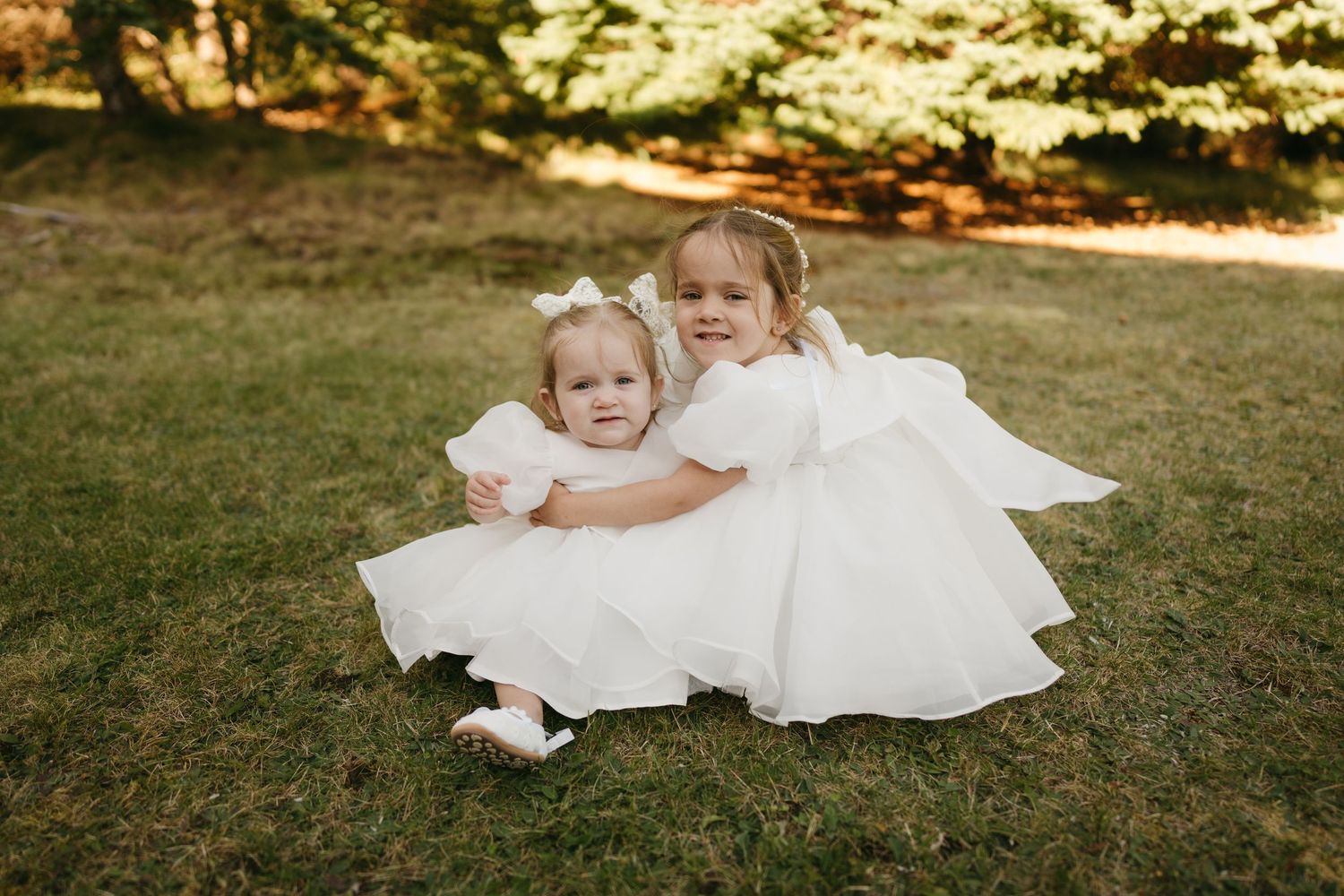 A person in a flowing white dress sits gracefully on grass during a golden hour outdoor photoshoot.