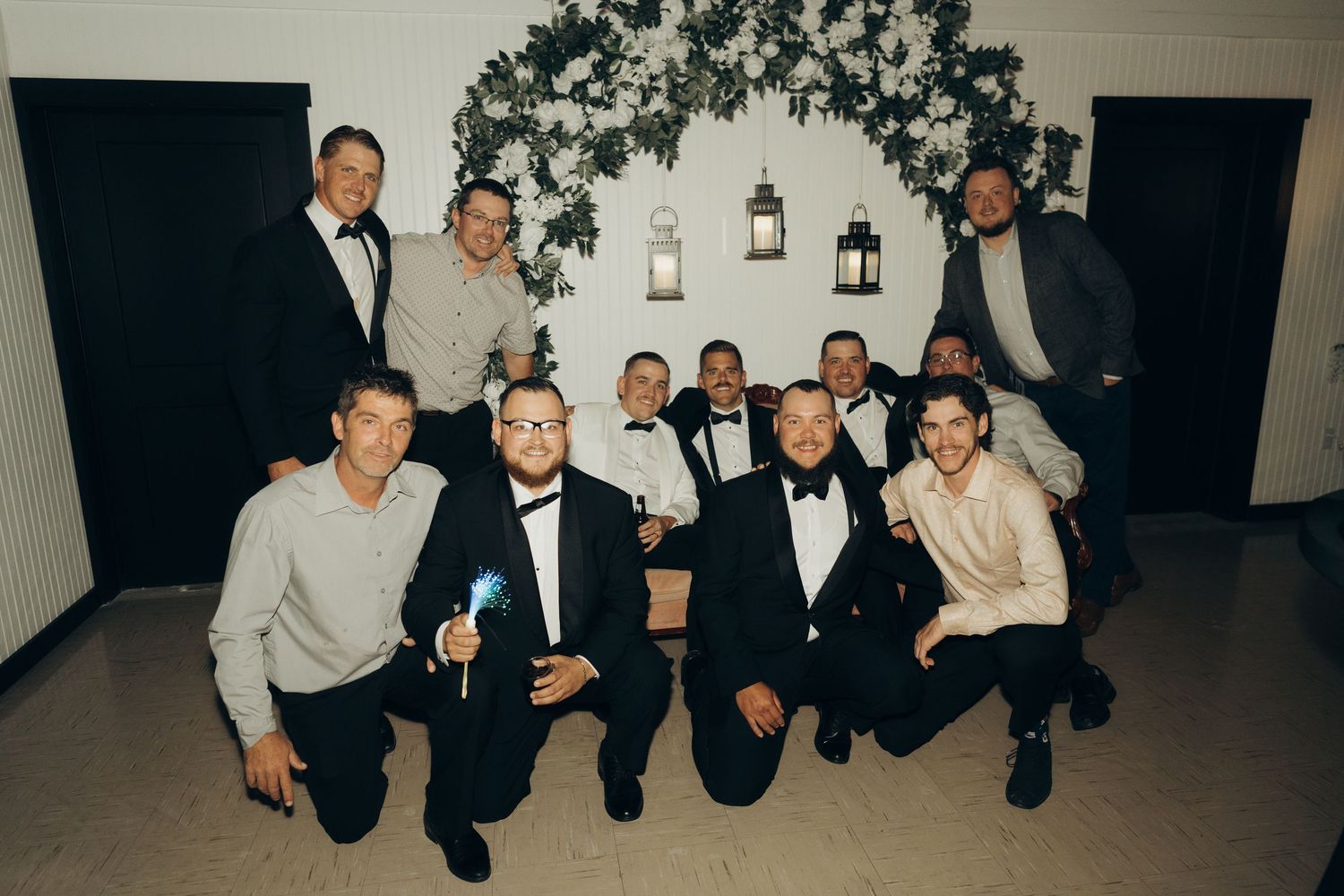 A group of people in formal attire pose together at a social gathering with lanterns visible in the background.