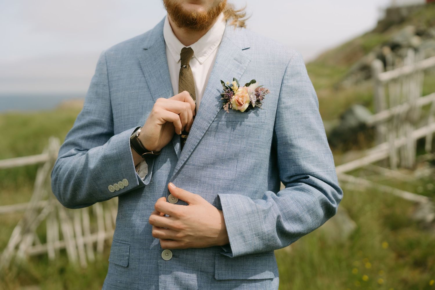 Close-up details of light blue suit jackets with boutonniere flowers at an outdoor wedding venue.