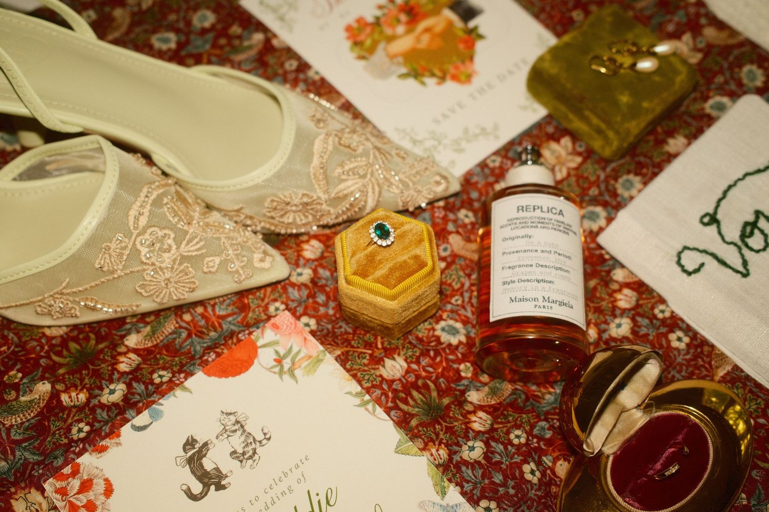 Flat bridal shoes, perfume bottle, ring boxes, and wedding stationery arranged on a floral rug.