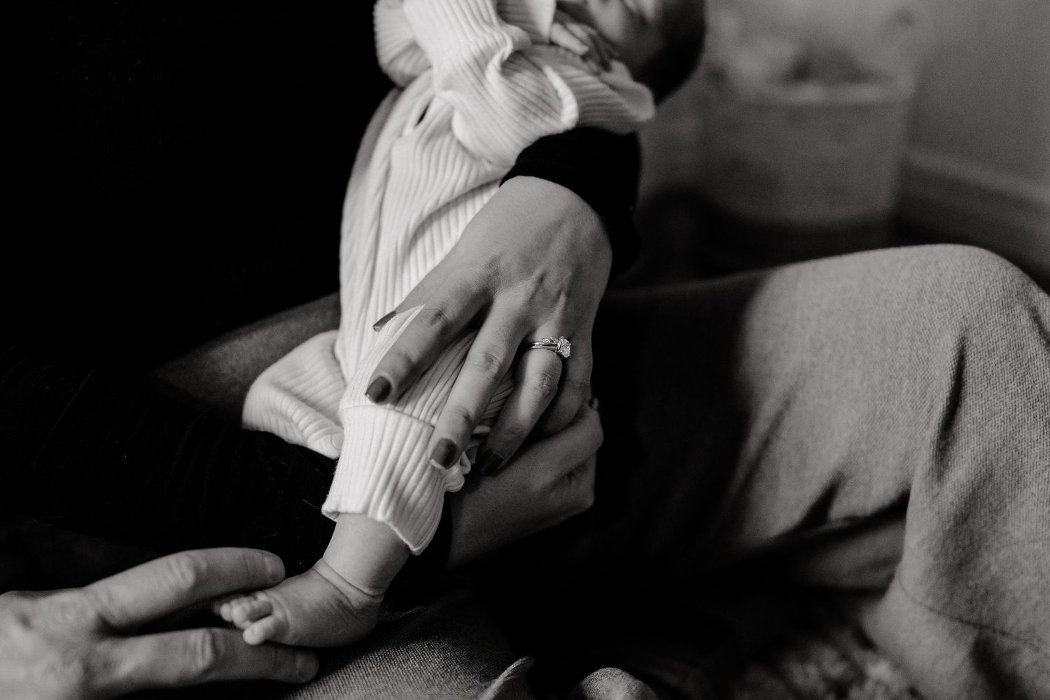 Black and white shot of a small baby being gently held on a textured surface.