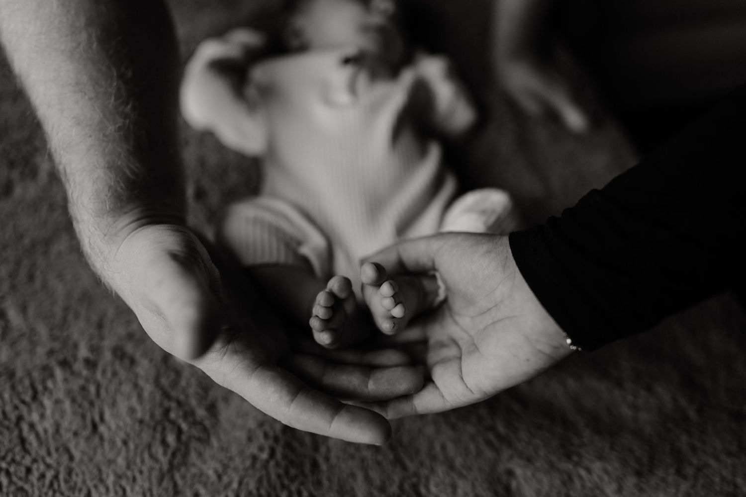 Artistic black and white capture of tiny infant hands being tenderly held.