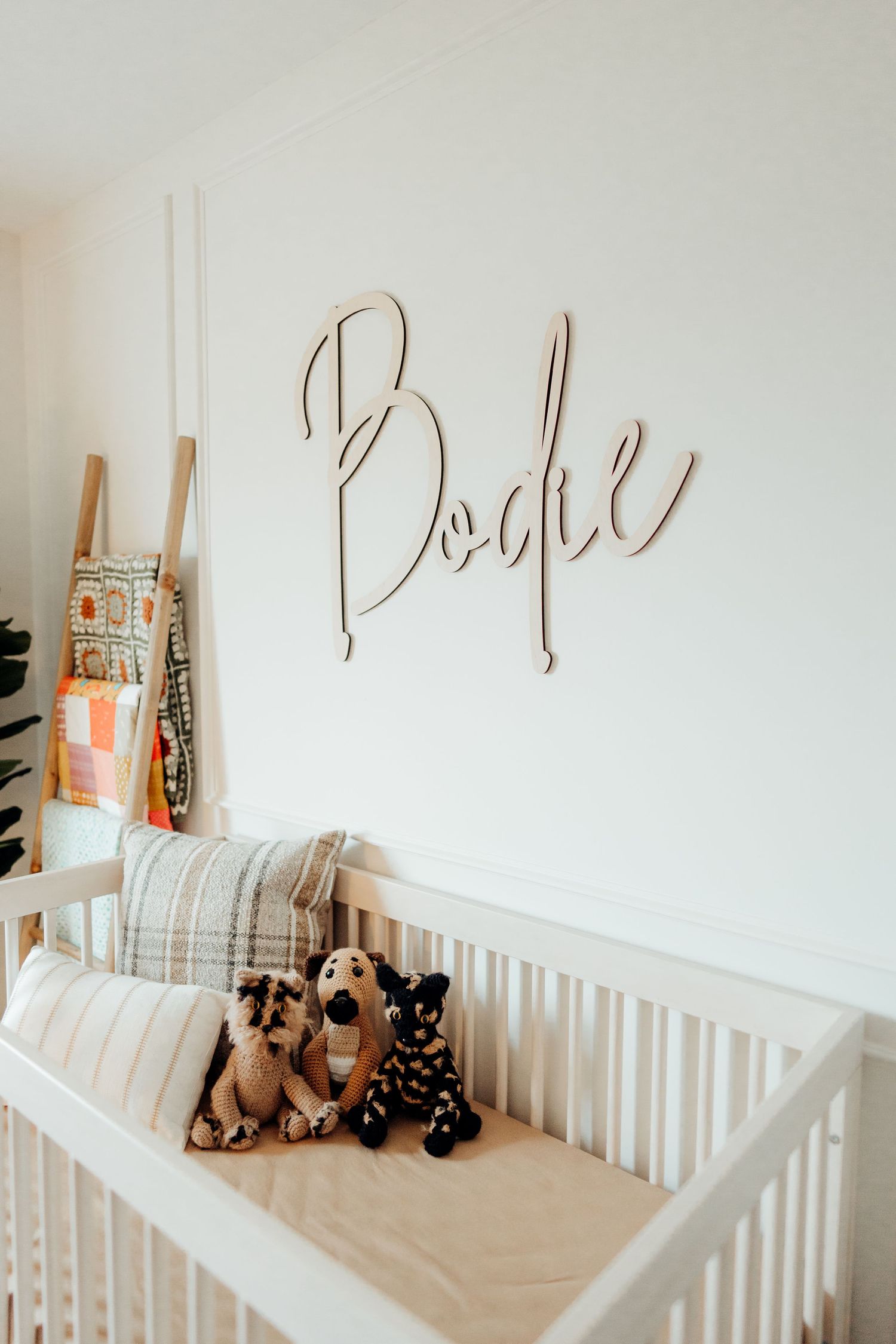 Minimalist nursery room with white crib, decorative wall text, and plush animal toys.