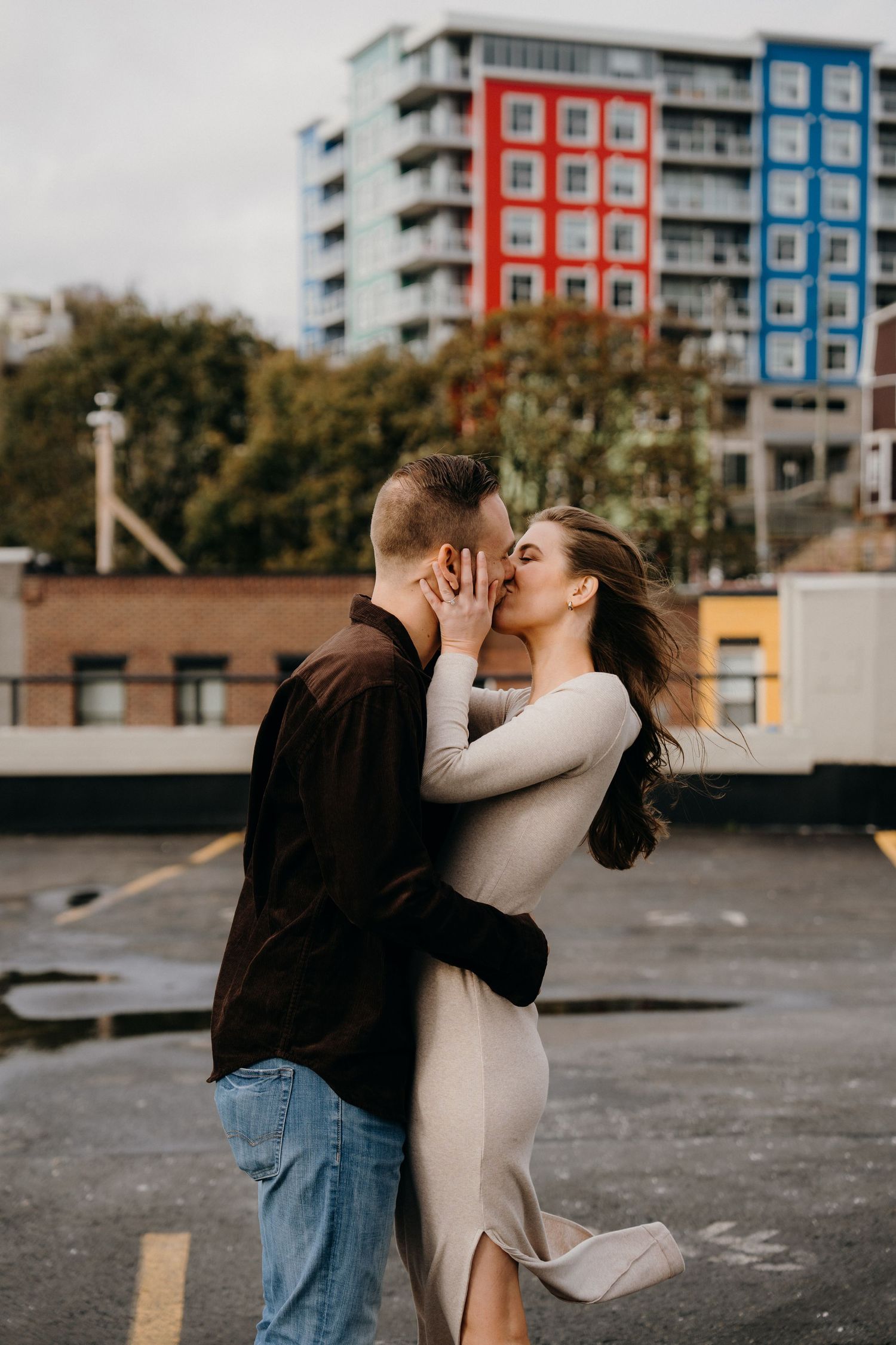A romantic embrace captured in front of modern apartment buildings on an overcast day.