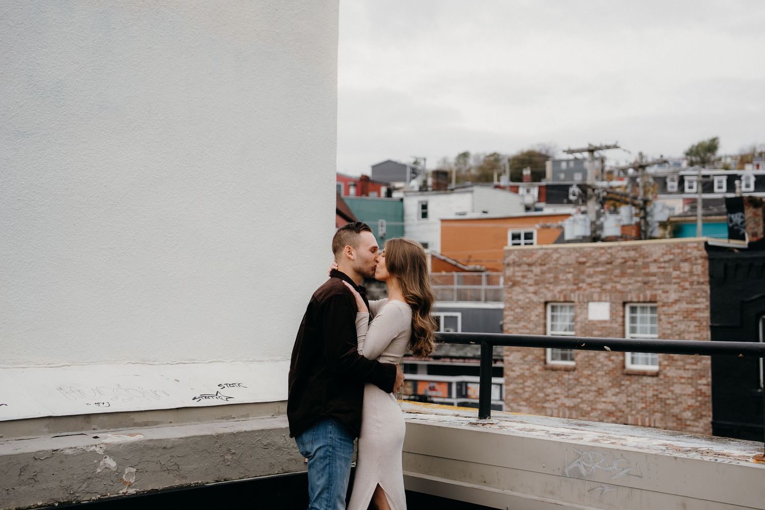 A couple sharing an intimate moment on a rooftop with city buildings in the background.