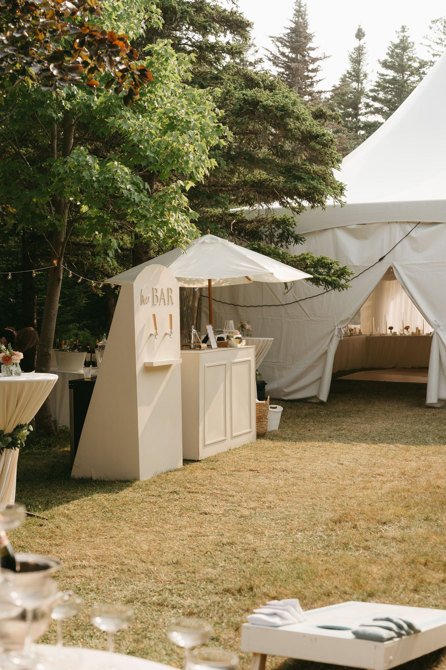 Row of white wedding reception tents set up in a wooded outdoor area.