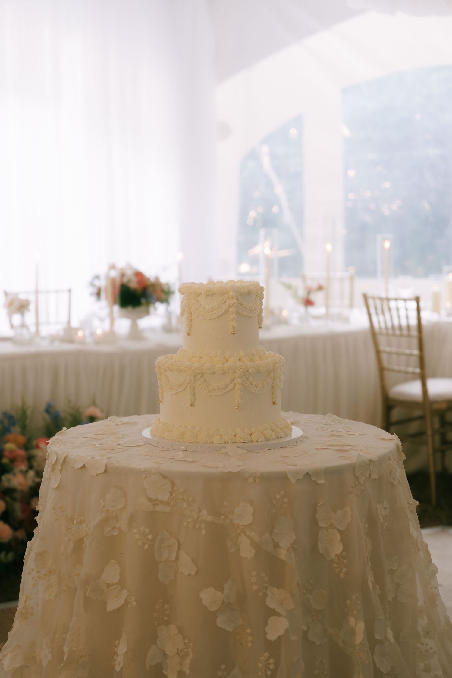 An elegant white wedding cake adorned with delicate details sits atop a decorative table with white linens.