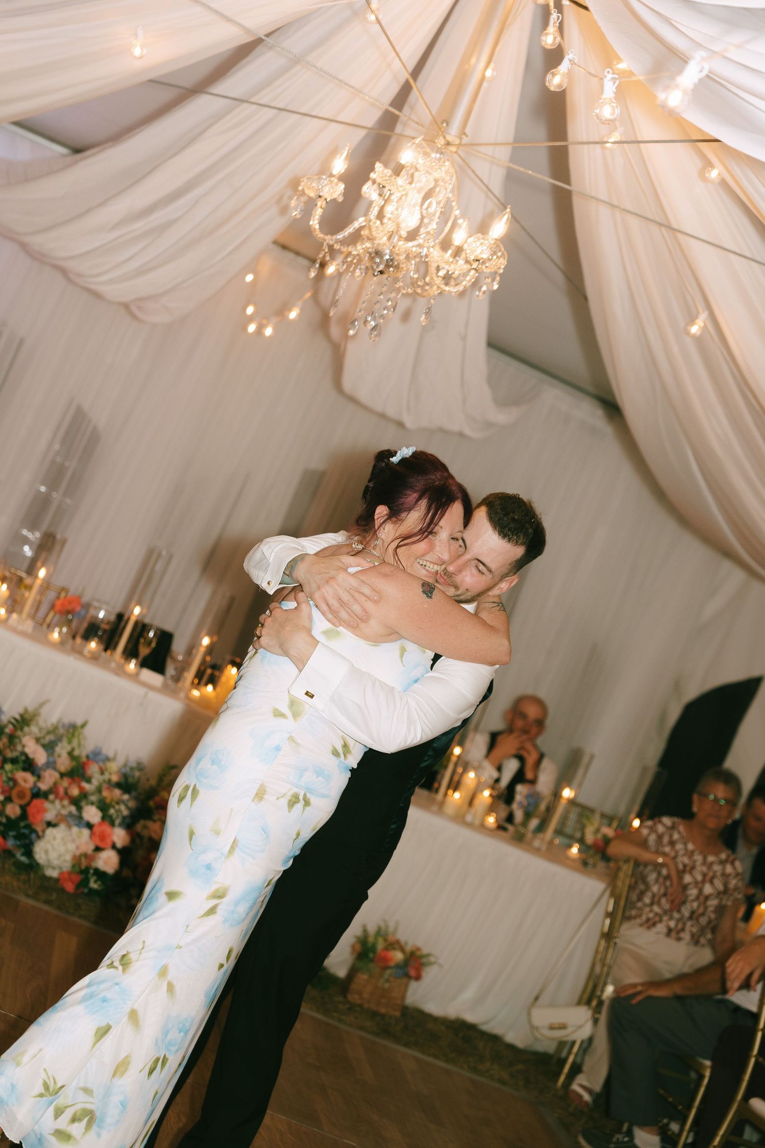 A romantic first dance moment in a draped reception hall with crystal chandeliers and soft lighting.