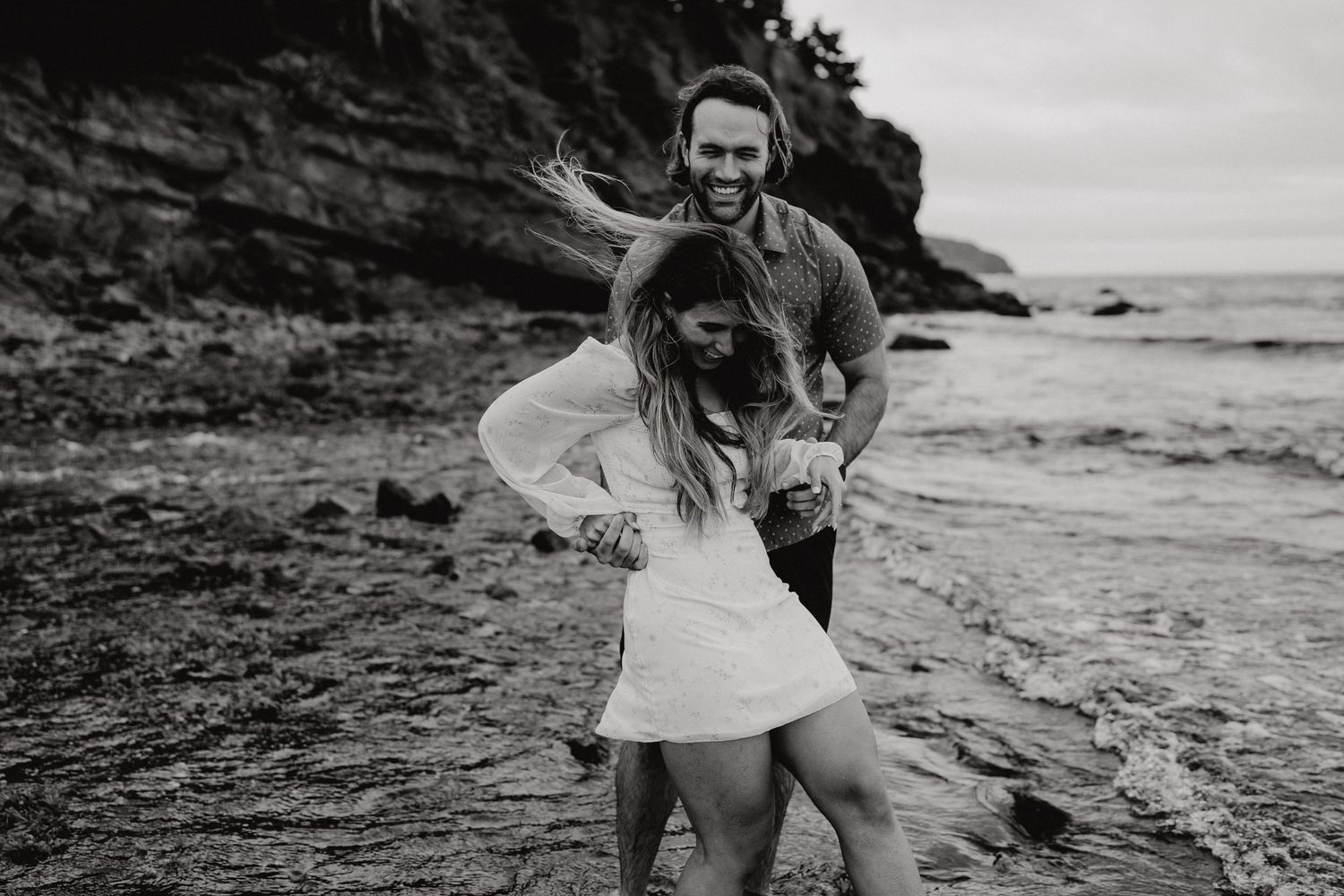 Couple exploring rocky coastal terrain during a cloudy day by the ocean.