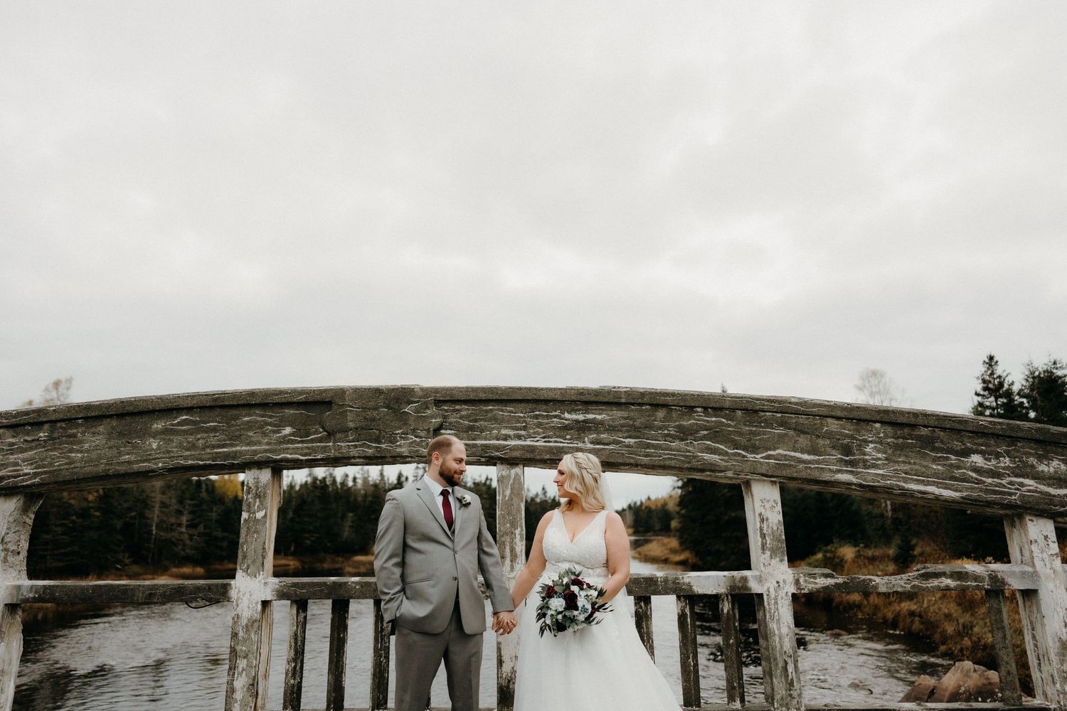 A couple stands against a rustic wooden backdrop on their wedding day.