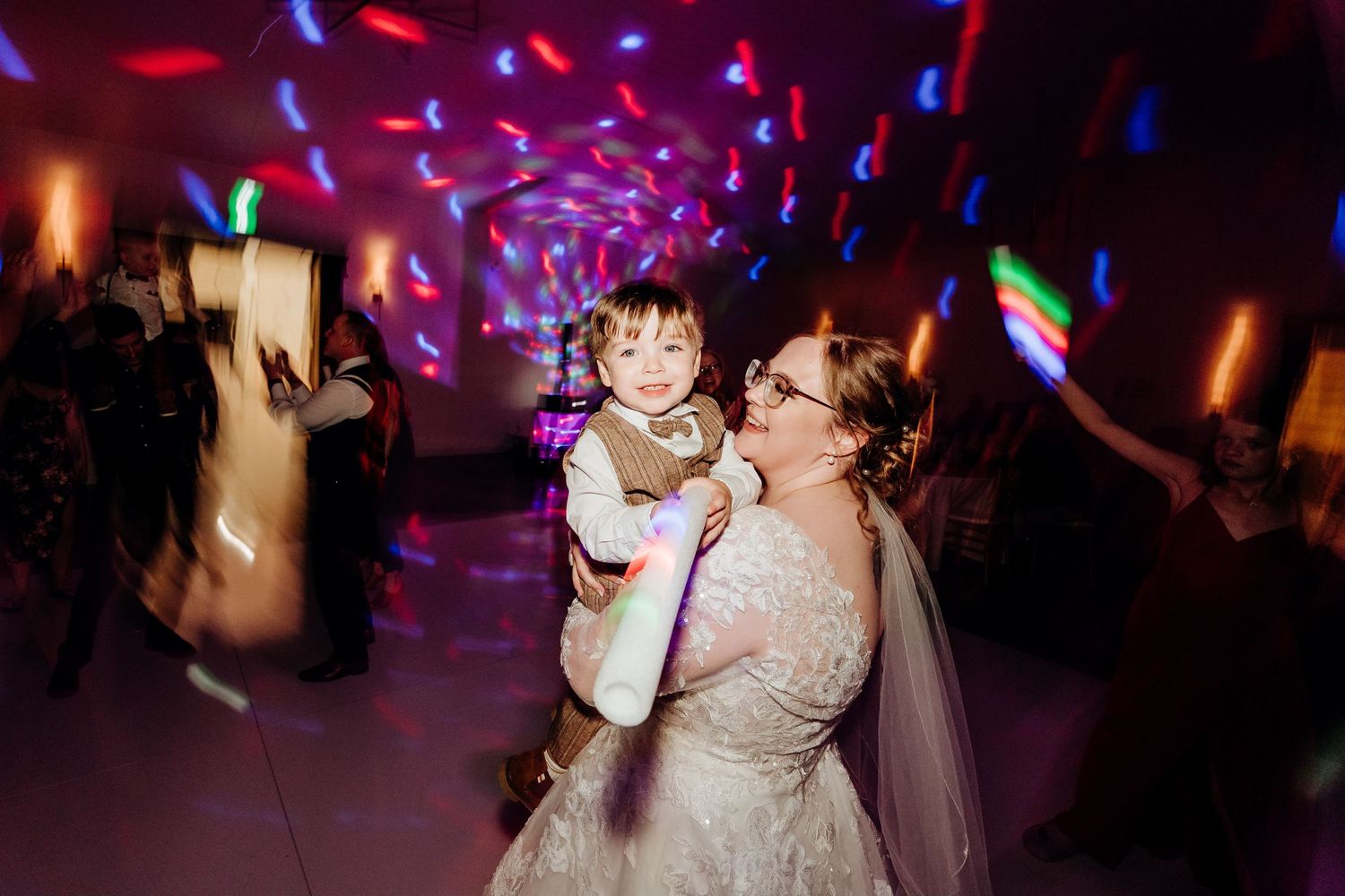 Wedding reception dance floor illuminated with vibrant purple and blue lighting.