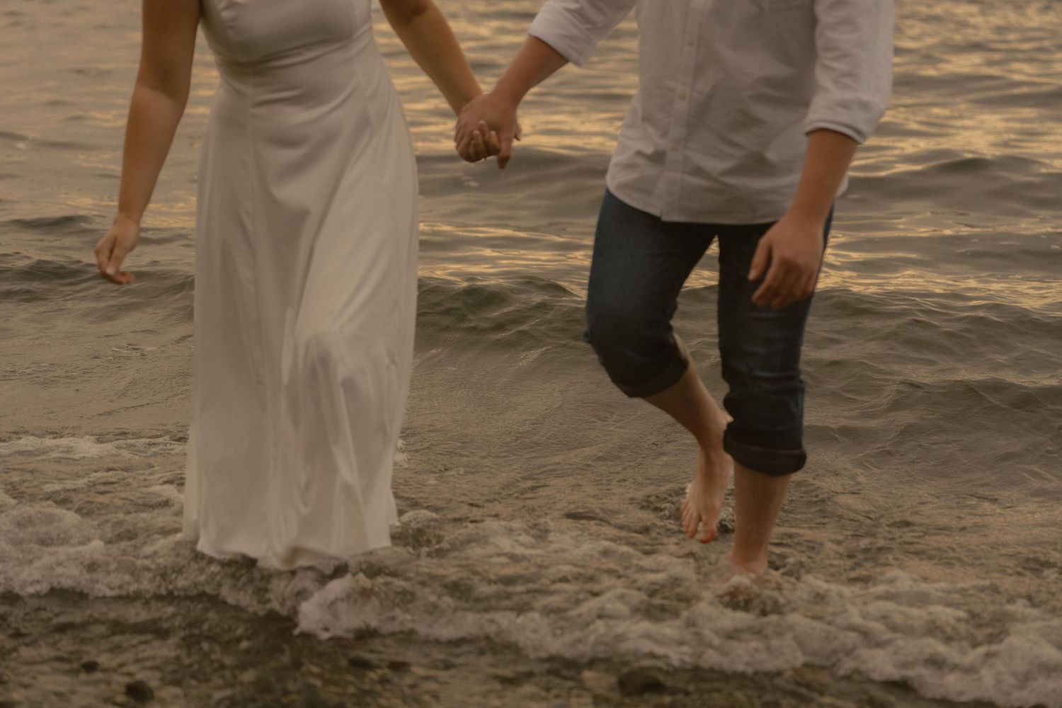 Romantic beach scene with couple's feet walking through gentle waves at golden hour.