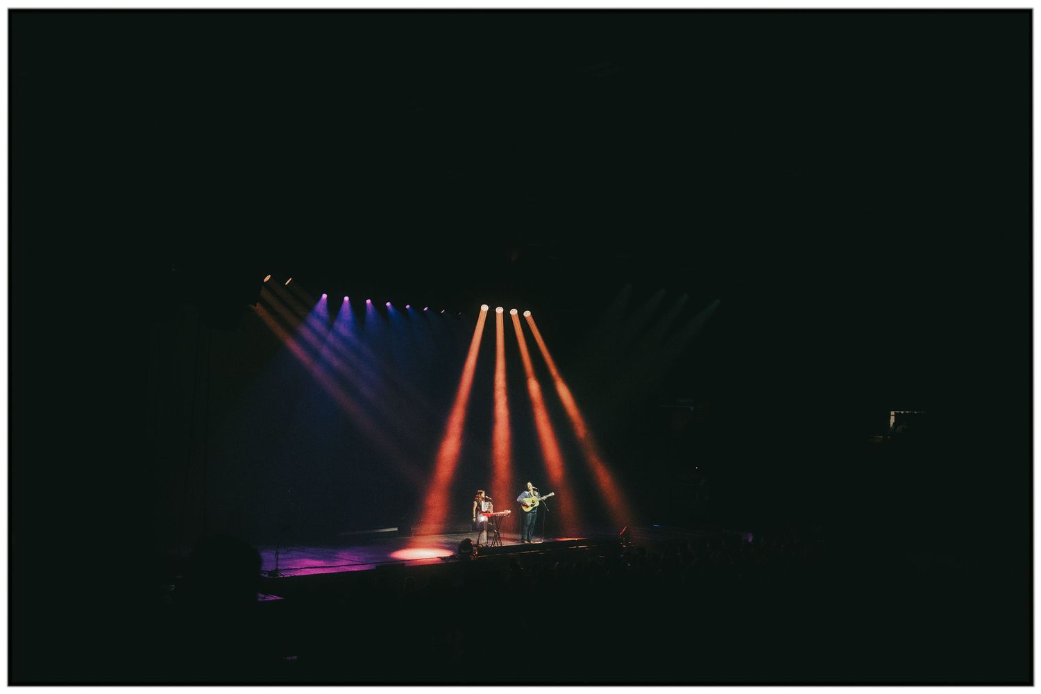 Dramatic stage lighting setup with colorful beams of orange and purple illuminating a dark performance space.