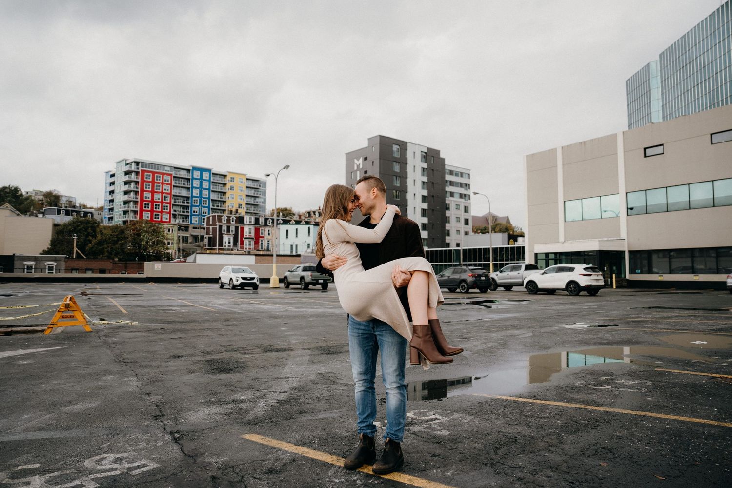 Couple performing a dip dance move in an empty concrete parking area surrounded by city buildings.