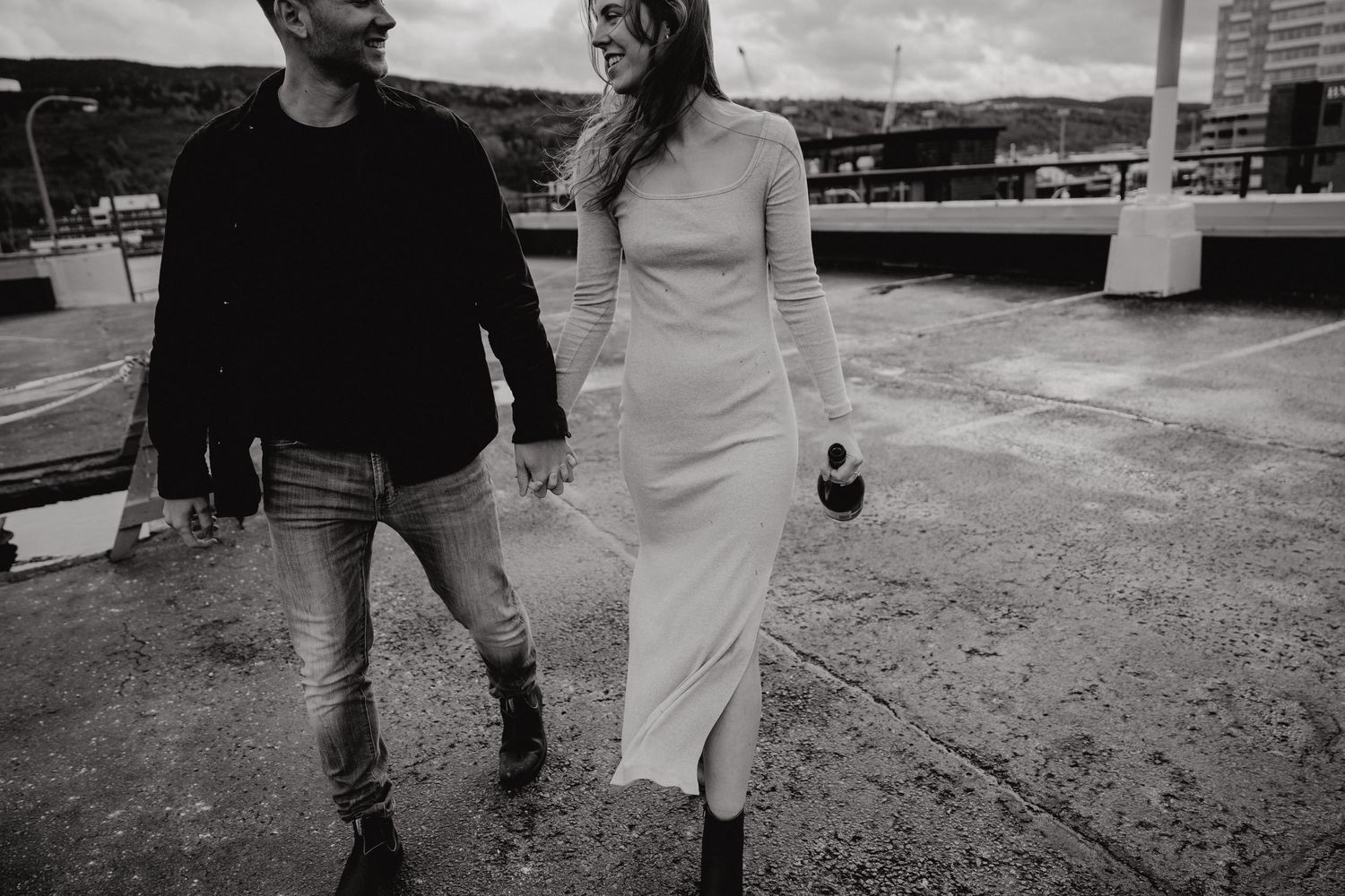 Black and white photo of couple walking together on industrial rooftop.