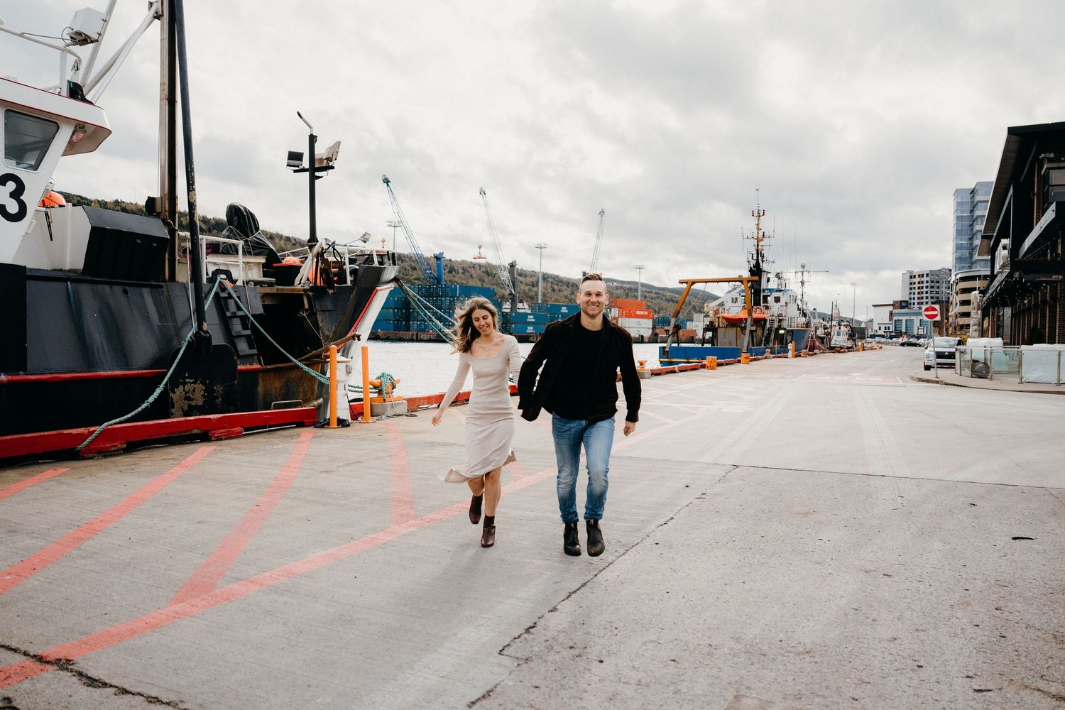 People strolling down a wide industrial pier with boats and harbor equipment visible.