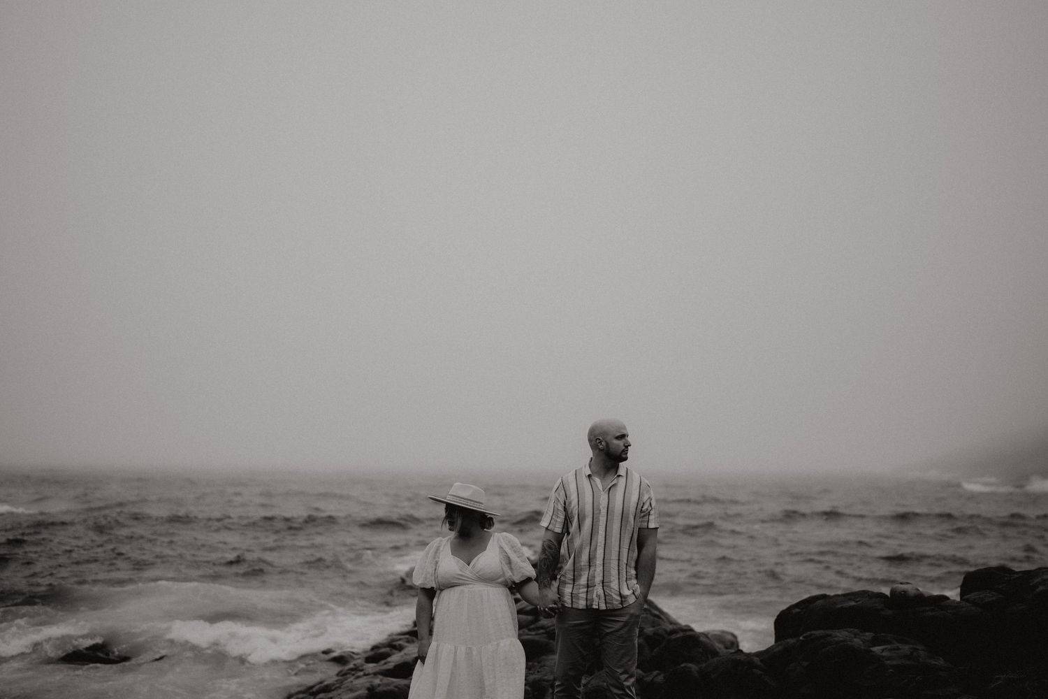 Misty gray ocean waves crash against a rocky shoreline under an overcast sky.