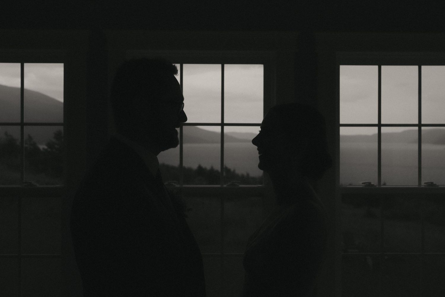 Dark silhouette of industrial buildings against overcast sky with dramatic moody lighting through windows.