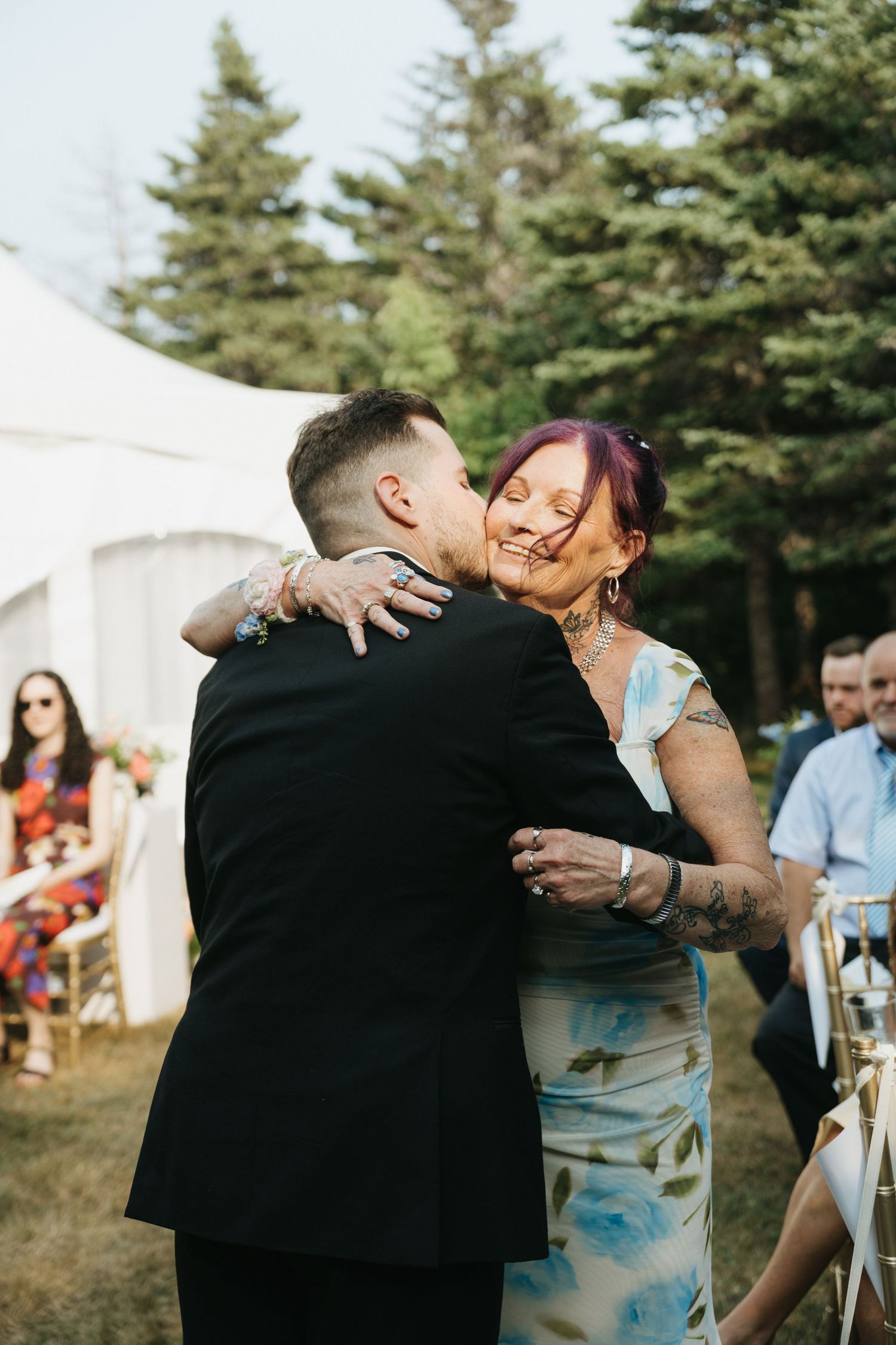 Wedding celebration with guests dancing in front of white tents and pine trees.