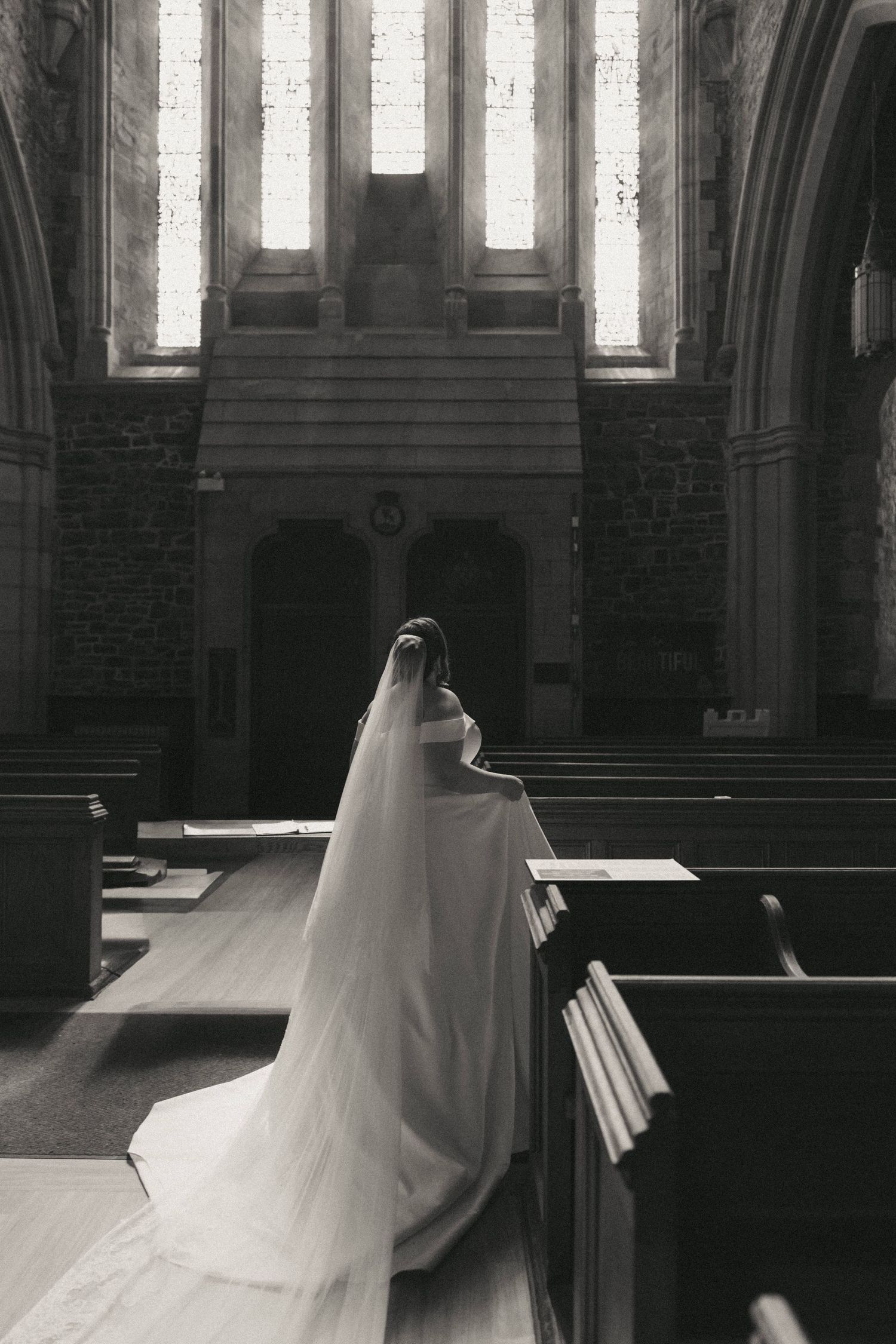 A flowing white wedding gown sweeps across the aisle of a grand church interior.