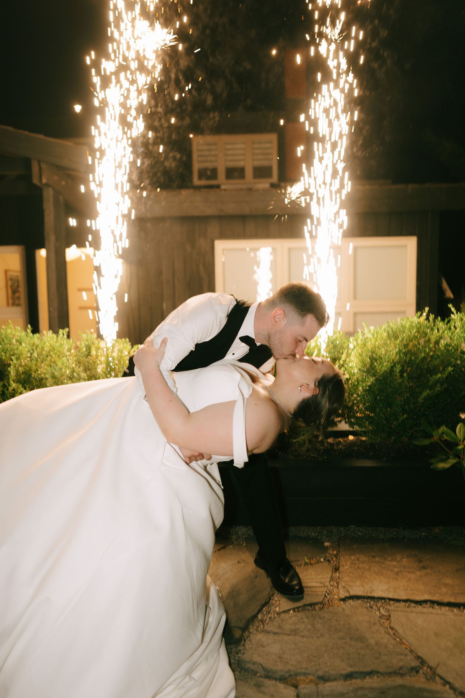 A couple shares their first dance outdoors with dramatic sparklers creating a magical backdrop at night.