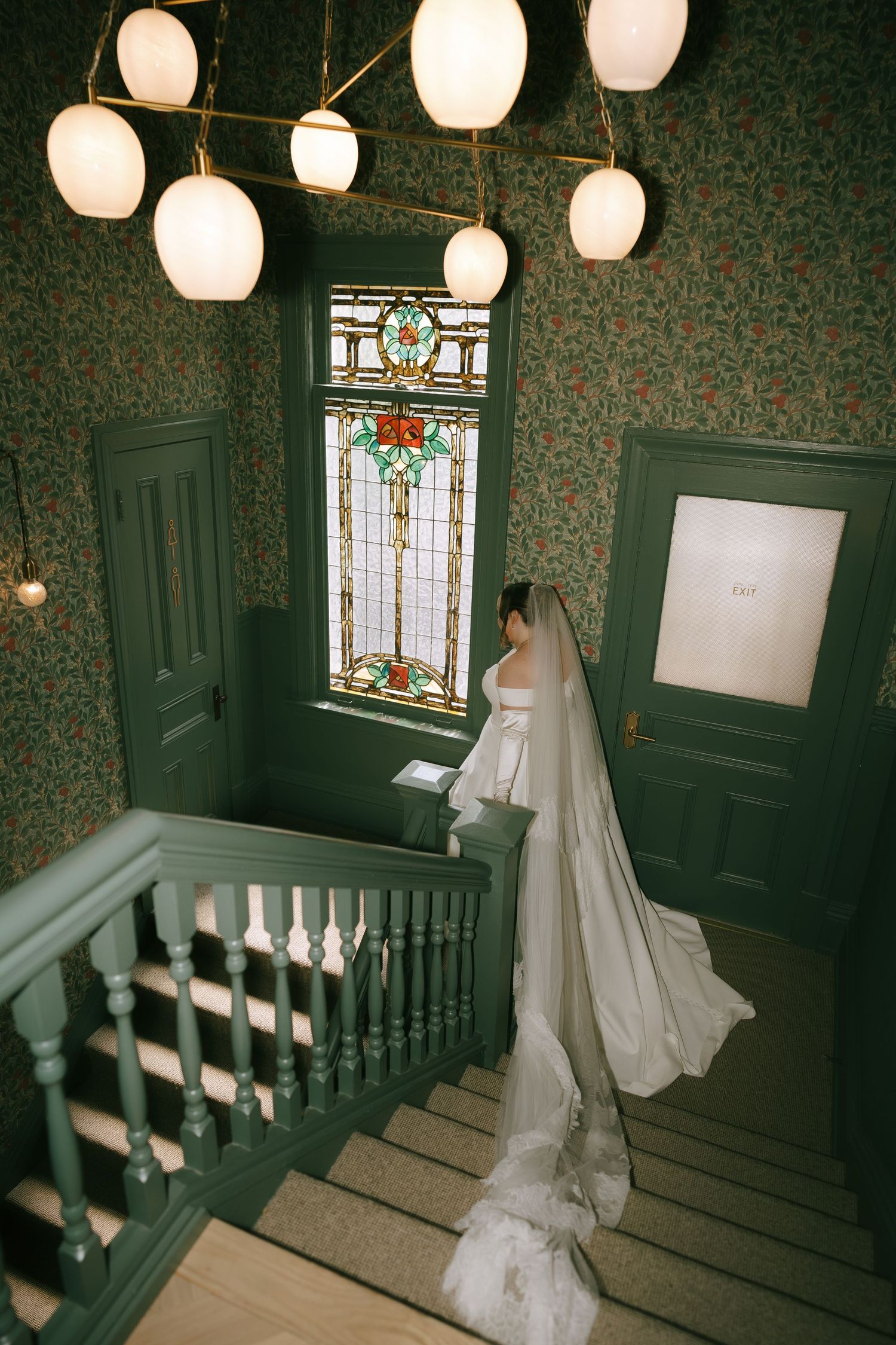 A wedding dress displayed in a vintage hallway with paper lanterns and stained glass windows.