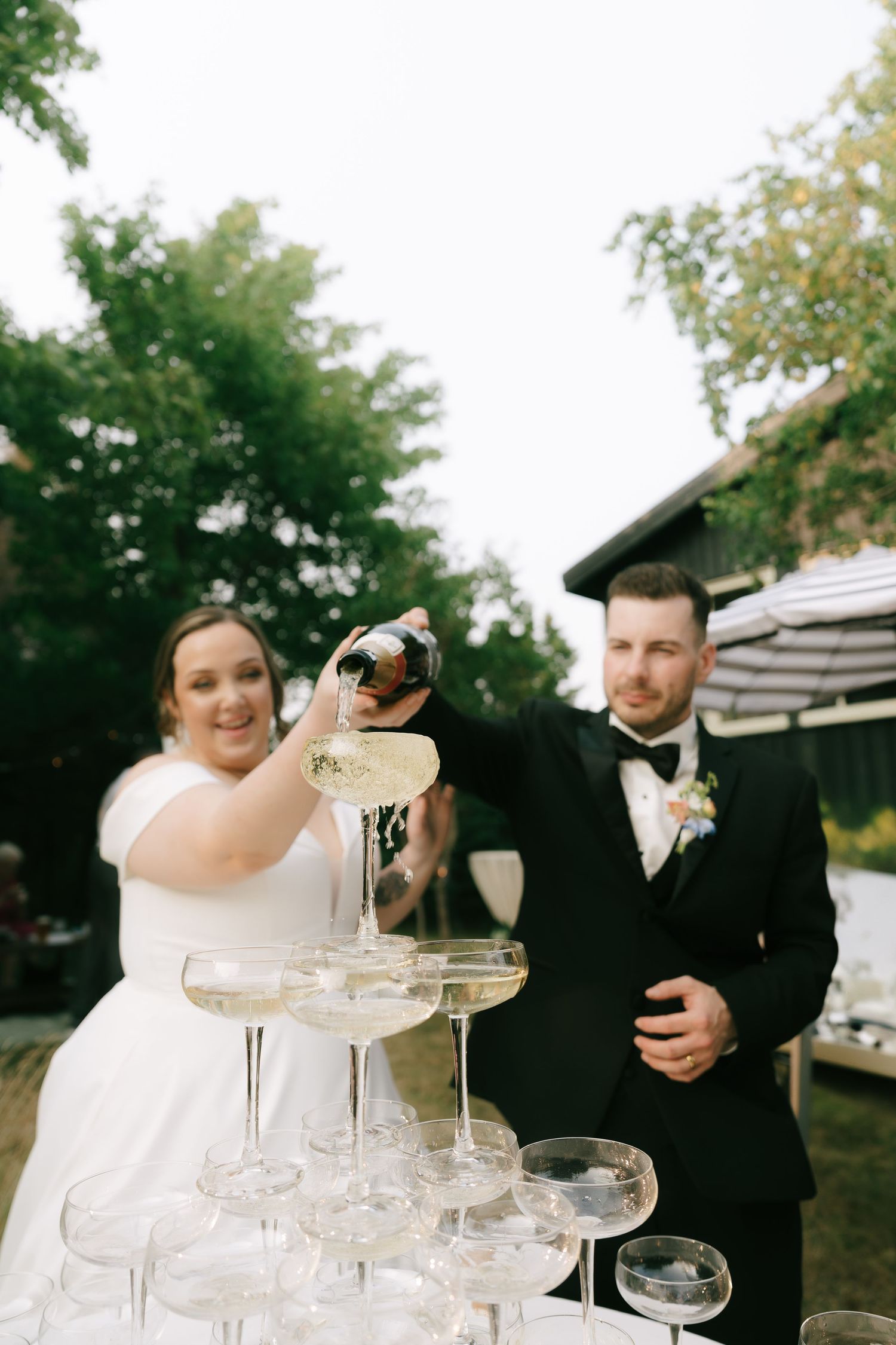 A couple pours champagne into a tower of crystal glasses during their wedding reception.