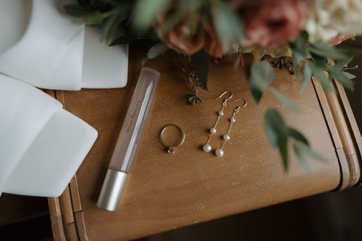 Wedding details including floral arrangements, rings, and decorative elements arranged on a wooden surface in warm lighting.