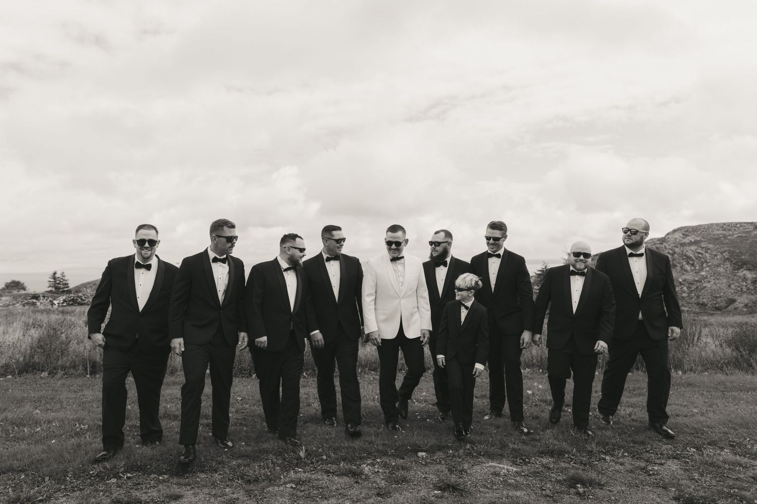 A group of people in formal black and white attire standing in a row outdoors against a desert landscape.