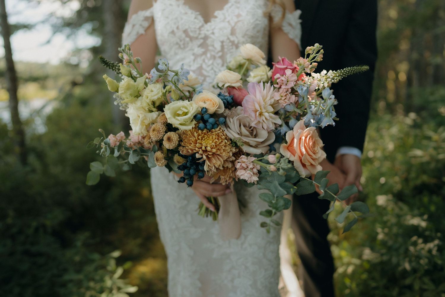 A beautiful bridal bouquet featuring soft peach roses, white flowers, and delicate greenery against a blurred outdoor background.