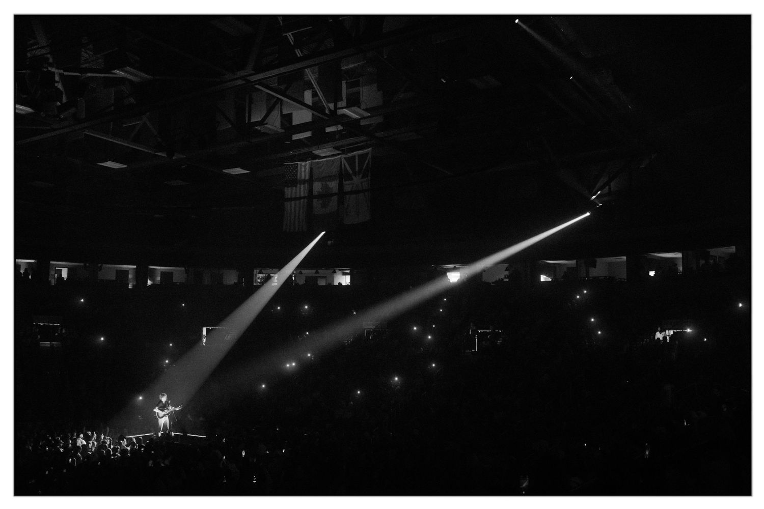 Concert stage illuminated by dramatic white spotlights against a dark background during a live performance.