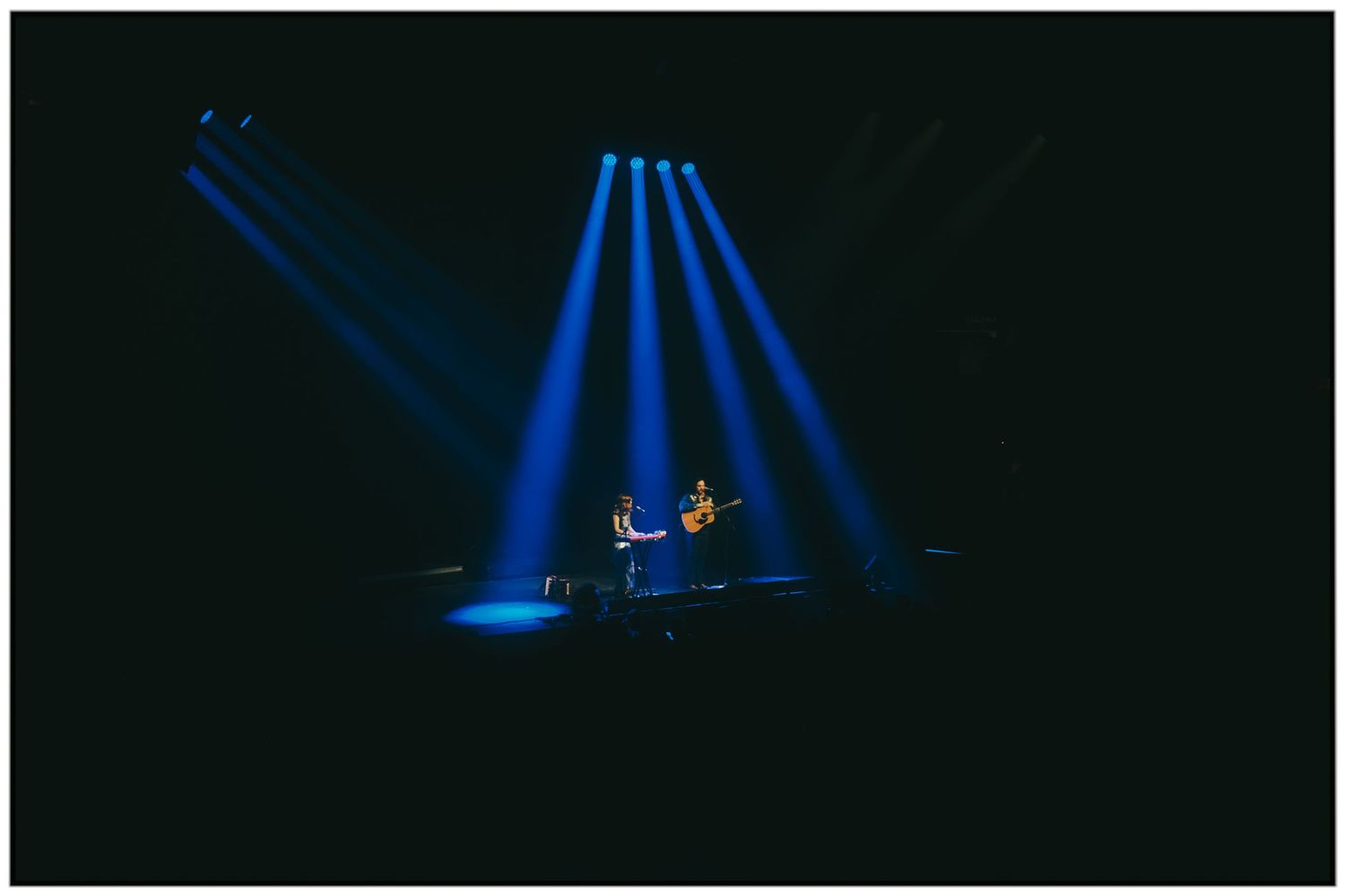 Blue spotlights illuminate a dark stage creating dramatic beams of light in a theatrical performance setting.