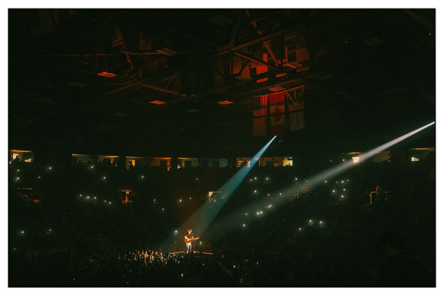 Concert crowd illuminated by dramatic red and blue stage lighting during a nighttime performance at an outdoor venue.
