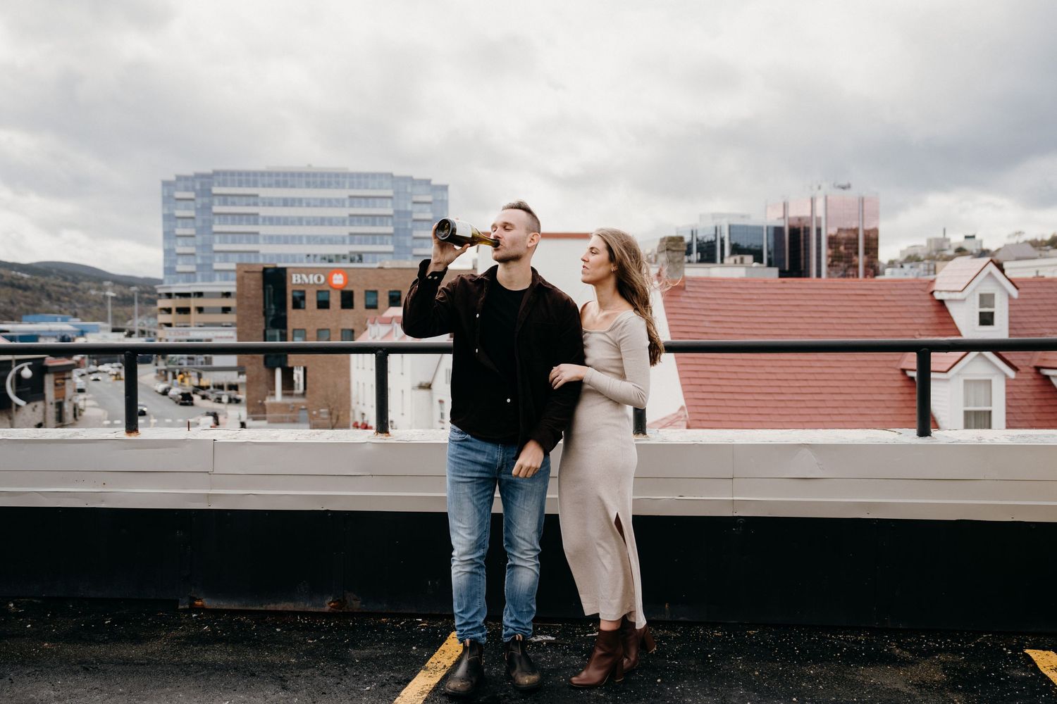 A couple stands close together on an urban rooftop terrace during an overcast day.
