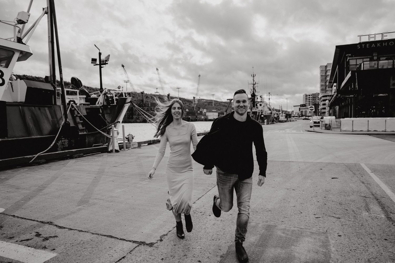 Two people walking together on a concrete pier at an industrial harbor.