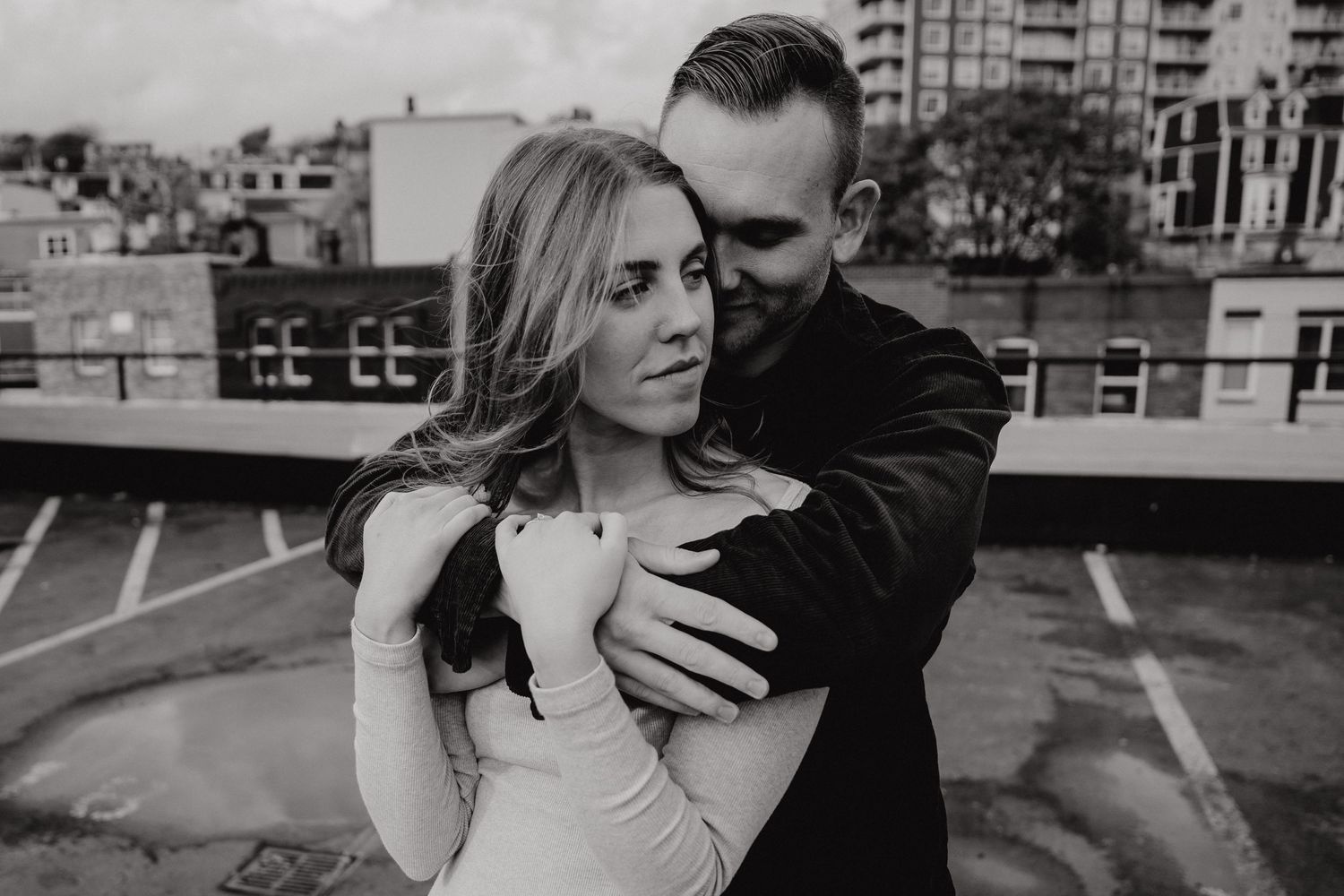 Romantic couple in black and white embracing on an urban rooftop with city buildings in background.