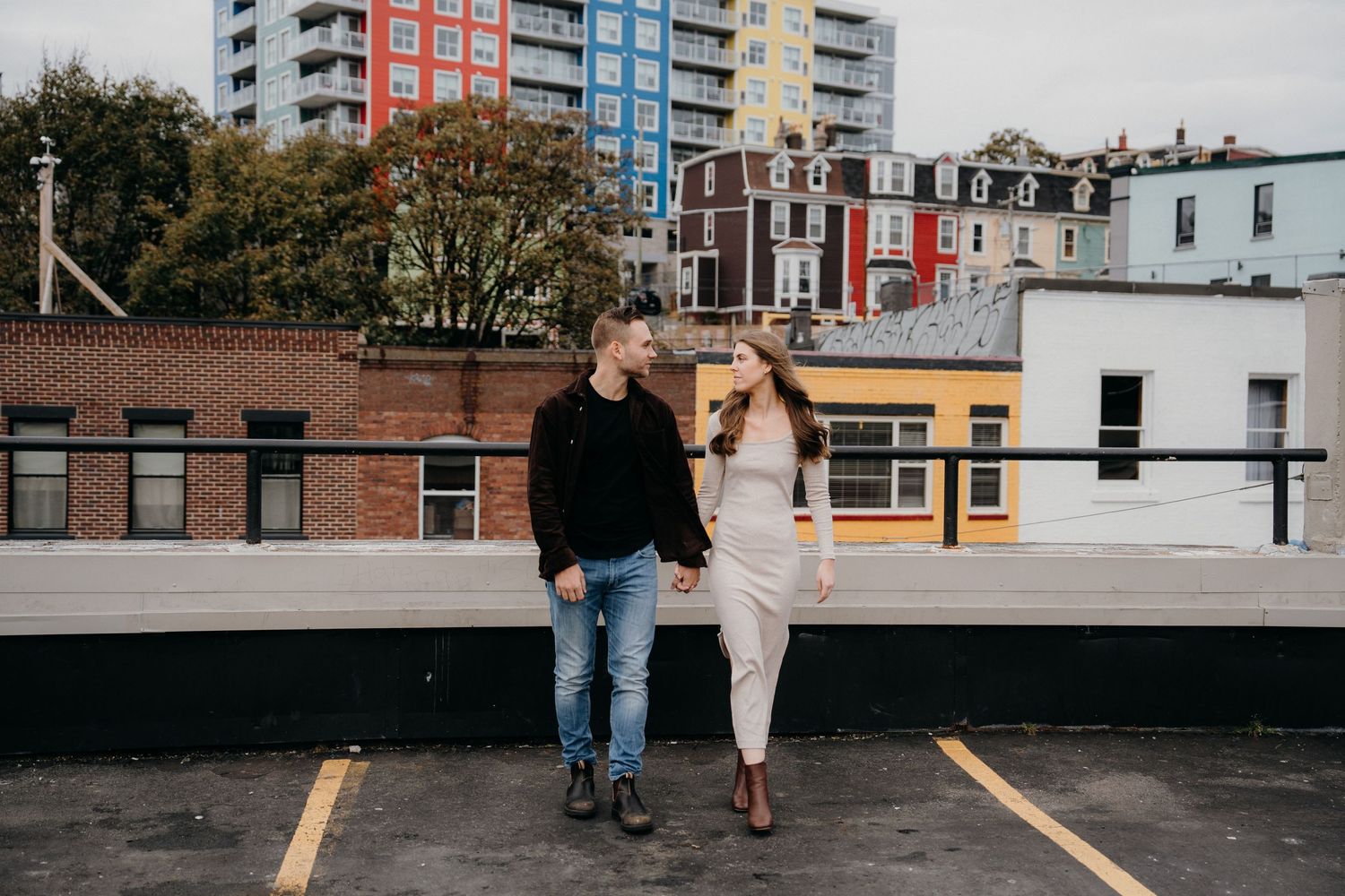 Urban rooftop engagement session with couple walking against city skyline.