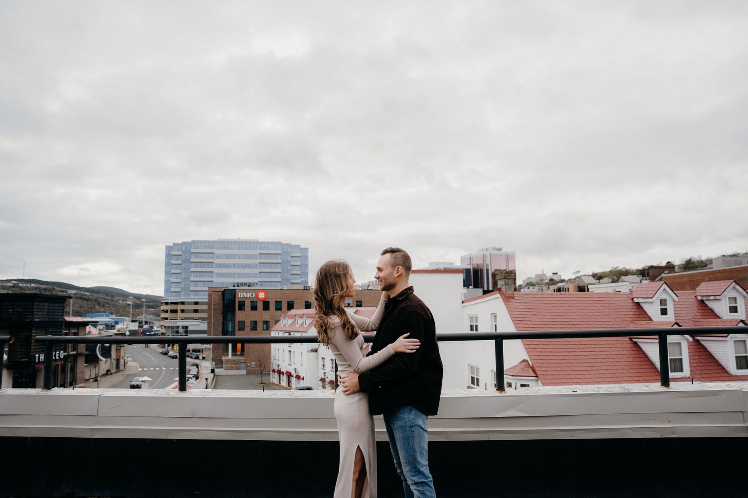 Wide shot of couple in urban setting with modern buildings and overcast sky.