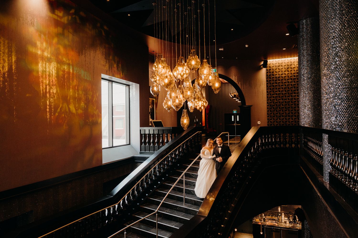 Moody wedding photography in dark venue with illuminated staircase and ambient lighting.